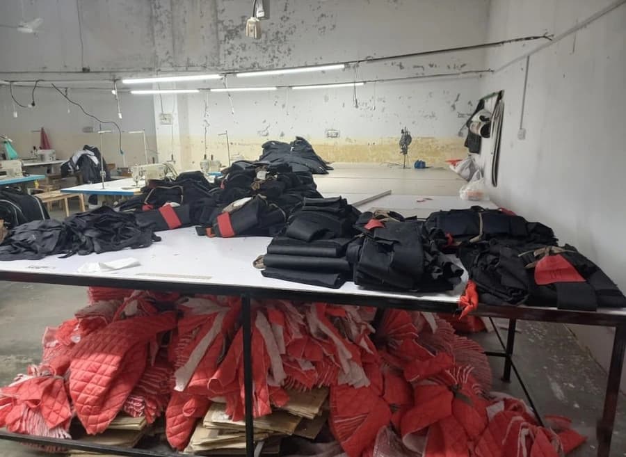Cut charcoal fabric panels tied into bundles with red size tape on a cutting table at the KBwear factory in Lahore, with red quilted lining stacked beneath