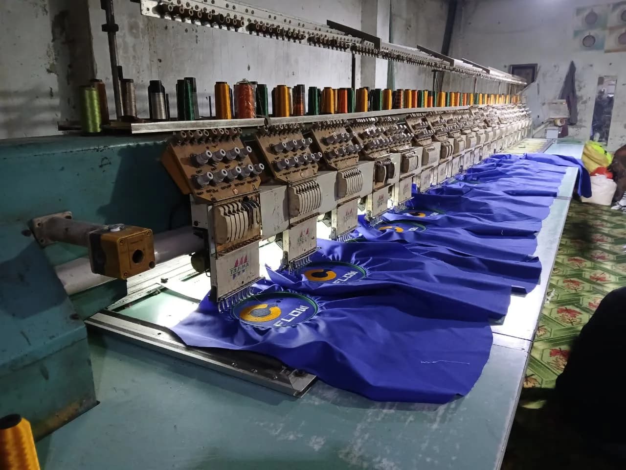 Multi-head embroidery machine running FLOW Petroleum logos onto royal blue uniform panels at the KBwear factory in Lahore